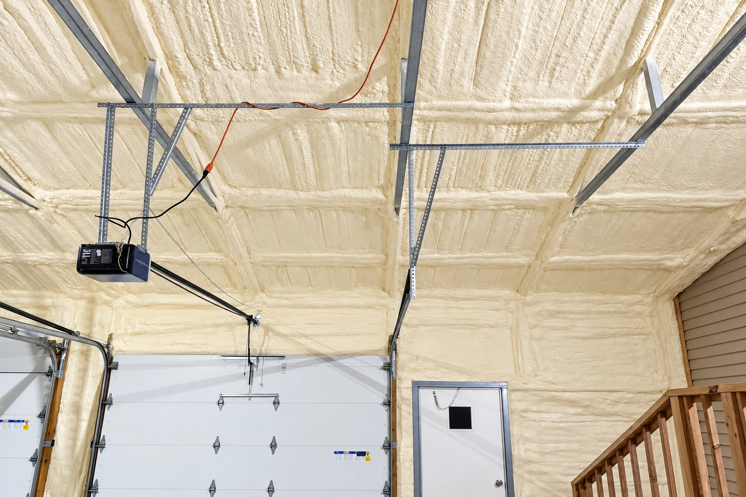 A garage interior has cream-colored spray foam covering the ceiling and walls around the garage doors.